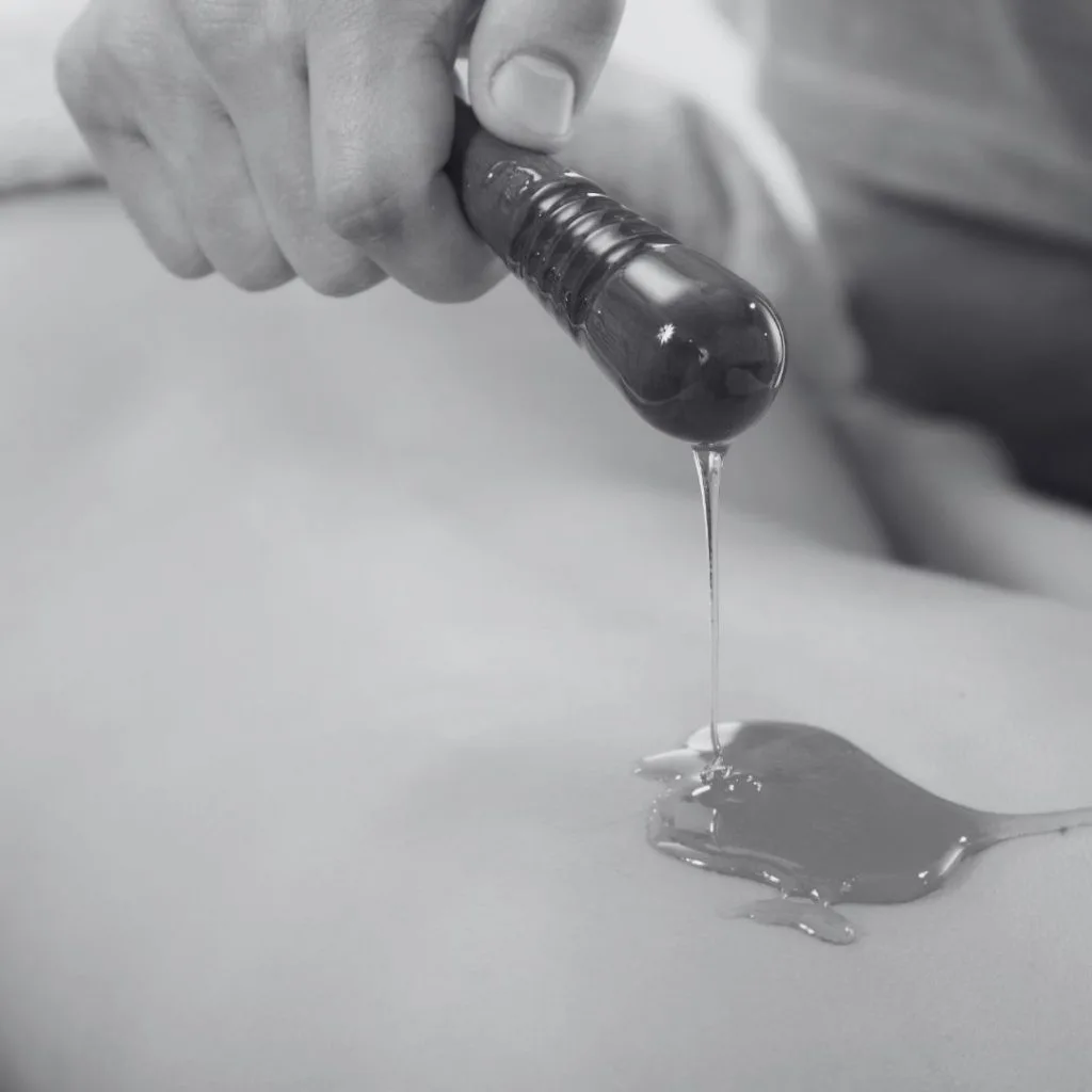 Main versant un liquide huileux sur la peau, gros plan noir et blanc